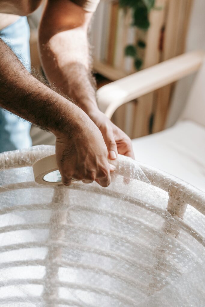 Close-up of a man wrapping a chair with bubble wrap indoors for moving or protection.