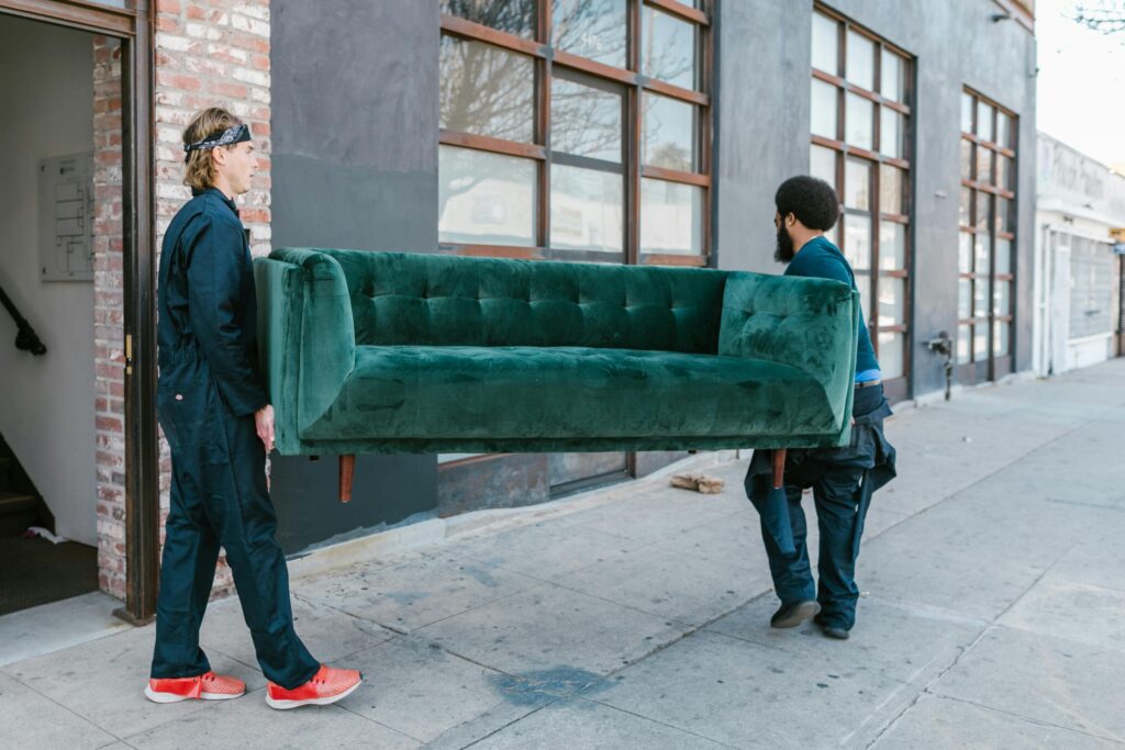 Two men carrying a green sofa on a city street, showcasing teamwork and moving services.